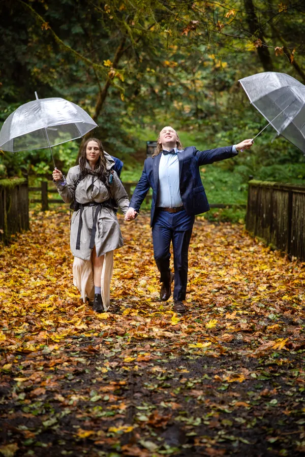 Couple dancing down an autumn path under clear umbrellas