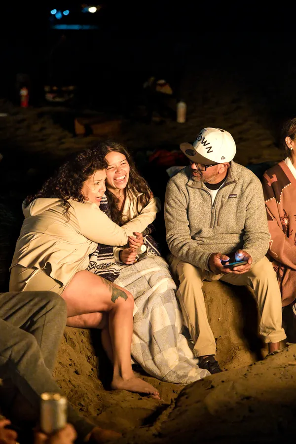 Friends wrapped in blankets around a beach bonfire